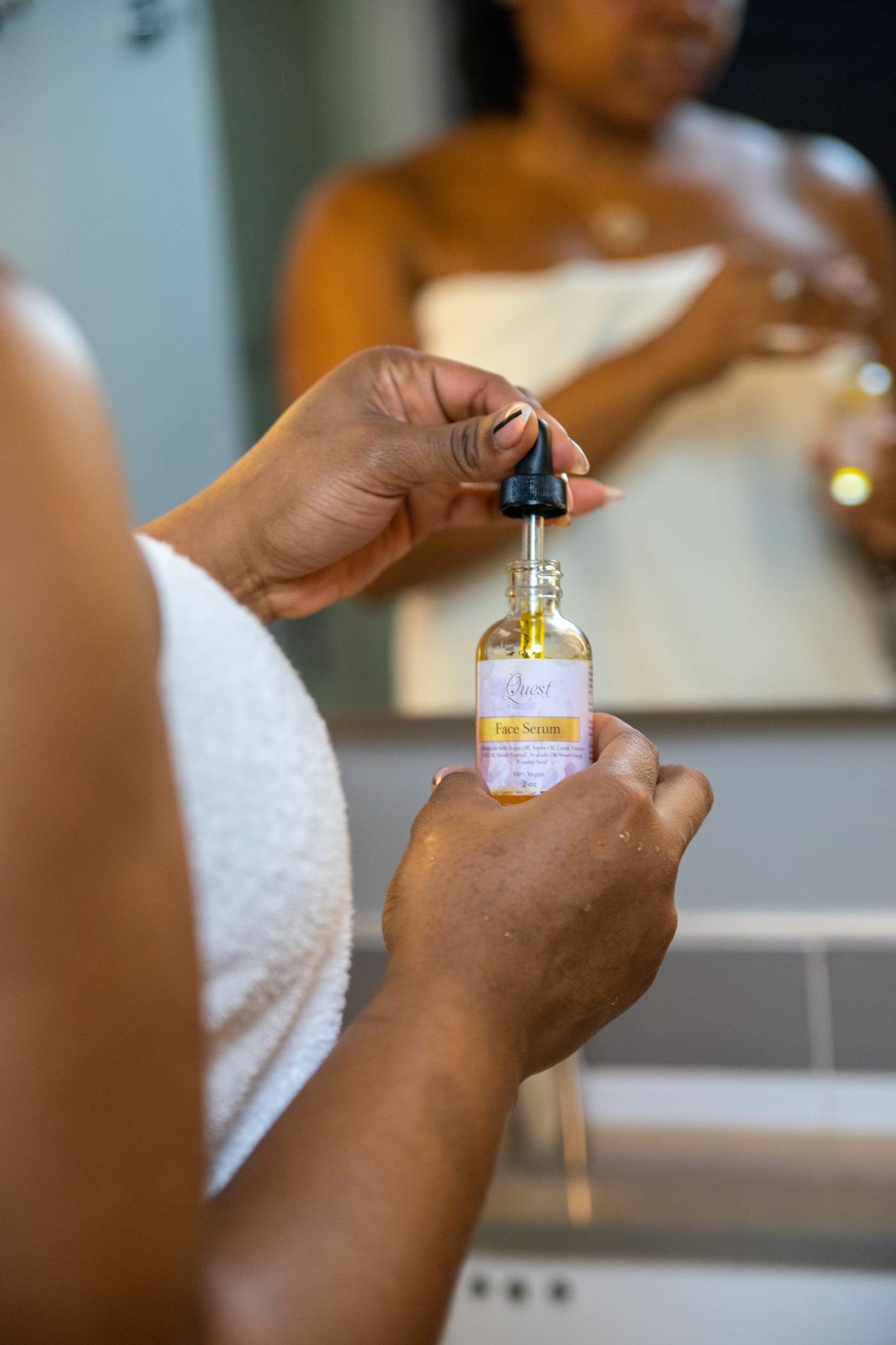 Person applying a dropper serum in front of a bathroom mirror